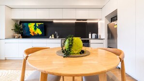 A modern kitchen with white cabinets, a large flat-screen TV, and a dining table with chairs. - Sydenham | Patio + Free Parking Near CBD (Christchurch)