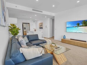 Ein modernes Wohnzimmer mit einer Couch, einem Couchtisch und einem Fernseher, der eine Strandansicht zeigt.