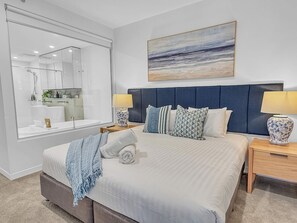 Une chambre à coucher moderne avec un grand lit, une tête de lit, deux tables de chevet, une commode, un miroir et un tableau accroché au mur.