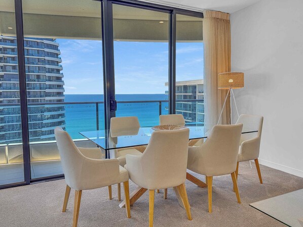 Une pièce moderne avec une table et des chaises en verre, un lampadaire et une vue sur l’océan et un immeuble de grande hauteur.