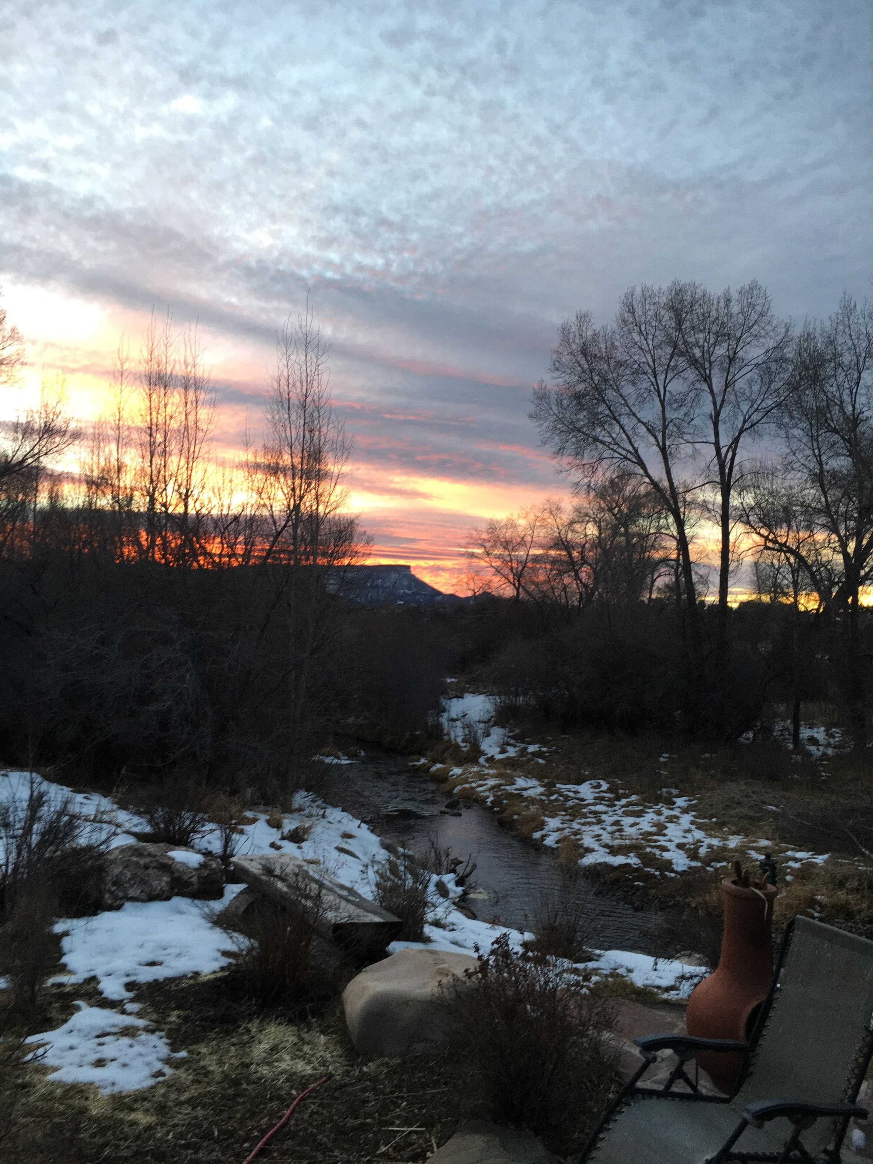 A bench overlooking a natural landscape with a river and trees, during sunset.