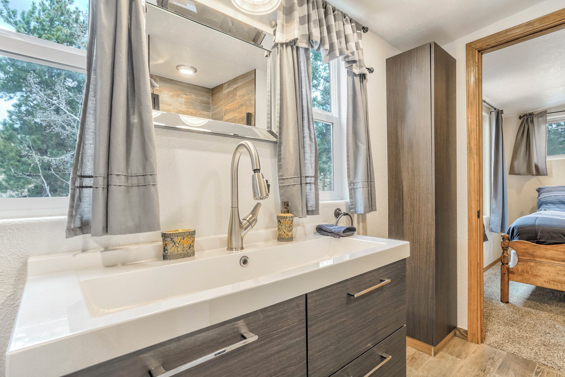 A modern bathroom with a large sink, two mirrors, and a window with curtains.