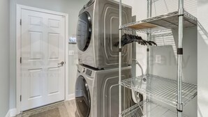 A laundry area with a front-loading washer and dryer, a white door, and metal shelving units. - 632 Palmetto Place - Wildlight (Indialantic)