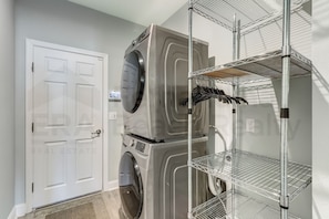 A laundry area with a front-loading washer and dryer, a white door, and metal shelving units. - 632 Palmetto Place - Wildlight (Indialantic)