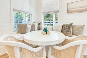 A round white table with a woven chair design, surrounded by cushioned seating with patterned pillows. - 133 Silver Laurel Way (Santa Rosa Beach)