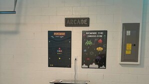 A room with a white brick wall, arcade-themed posters, a podium, and two bar stools. - 333 Burford Circle Davenport (Davenport)