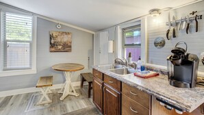 Una cocina con armarios de madera, encimera de mármol, cafetera y ventana con persianas.