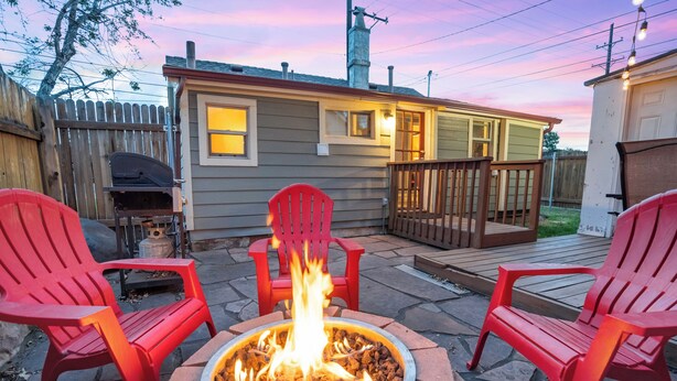 Un patio trasero con un pozo de fuego, sillas Adirondack rojas, una parrilla de barbacoa y una terraza de madera.