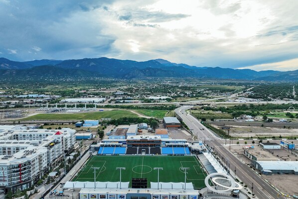 A stadium with a green field, surrounded by buildings and roads, with mountains in the background. - 15 E Las Animas St (Colorado Springs)