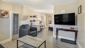 Una sala de estar con un televisor de pantalla plana, un sofá, una mesa de centro y un escritorio con una silla.