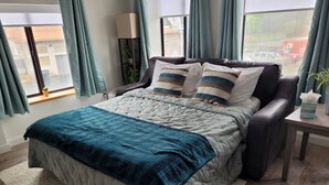 Une chambre à coucher avec un lit, une table de chevet, une lampe et une fenêtre avec des rideaux.
