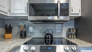 A kitchen with a stainless steel microwave, a kettle, and a stove with a digital clock. - 23 Magnolia, Rydal (Rydal)