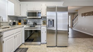 A modern kitchen with white cabinets, stainless steel appliances, and a granite countertop. - 23 Magnolia, Rydal (Rydal)
