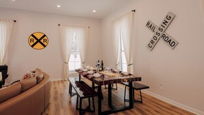 Un comedor con mesa de madera dispuesta para cuatro personas, sofá de cuero y ventana con cortinas.