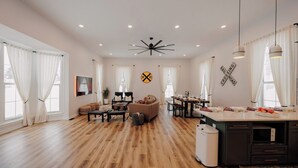 Amplia sala de estar con piso de madera, un sofá, una mesa de comedor y una zona de cocina con pileta y encimera.
