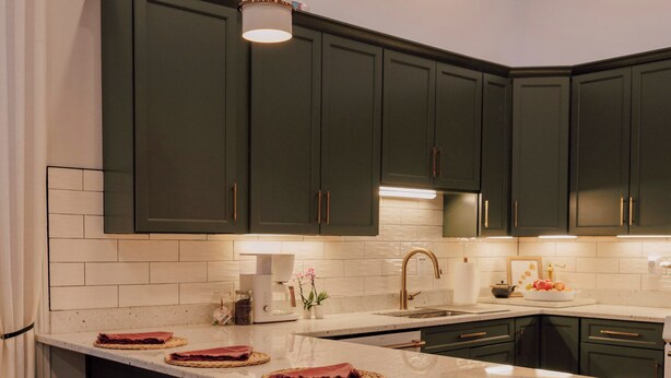 Una cocina moderna con armarios verde oscuro, encimera blanca y una isla central con taburetes.