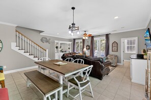 A spacious living area with a wooden dining table, white chairs, a brown leather sofa, and a kitchen area with a white countertop. - Nemos Reef | Coastal Retreat Near Surfside Pier (Surfside Beach)