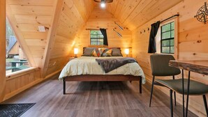 A cozy wooden cabin bedroom with a bed, two bedside lamps, a window, and a ceiling fan.