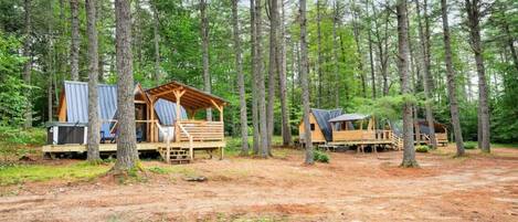 Un camping arbolado con cabañas de madera, cada una con terraza y zona de estar cubierta.