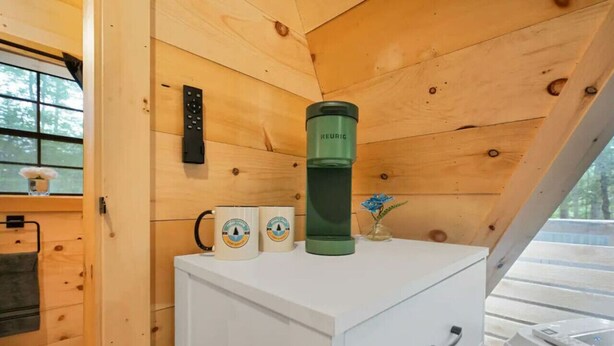 A wooden cabin interior with a white cabinet, a green thermos, and two mugs on top.