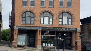 Un bâtiment en briques de deux étages, avec une enseigne indiquant « Kirk-Maher Co. » et « Café Nouveau » au rez-de-chaussée.