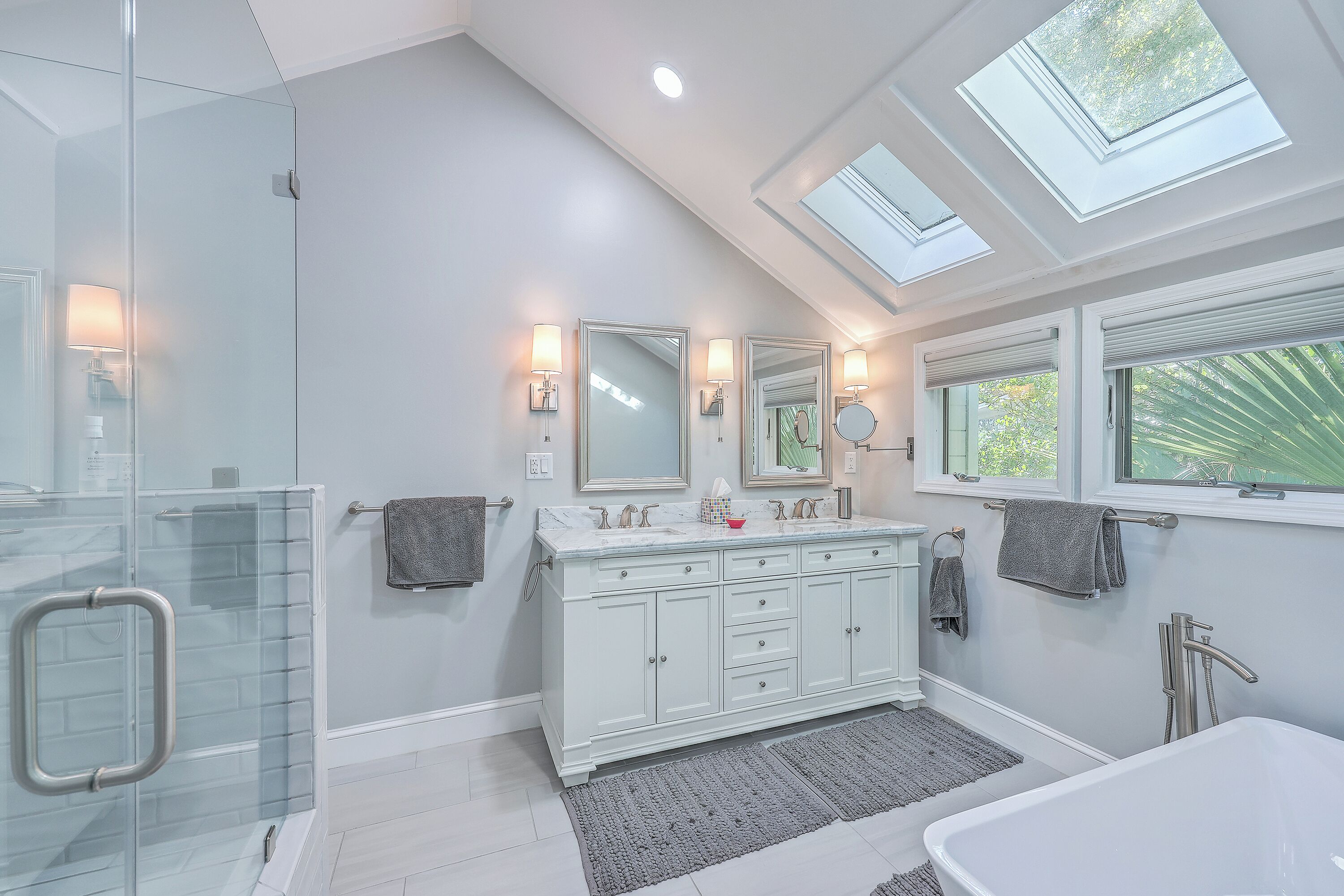 A modern bathroom with a glass shower enclosure, a walk-in shower, a large vanity with a mirror, and a skylight above the vanity.