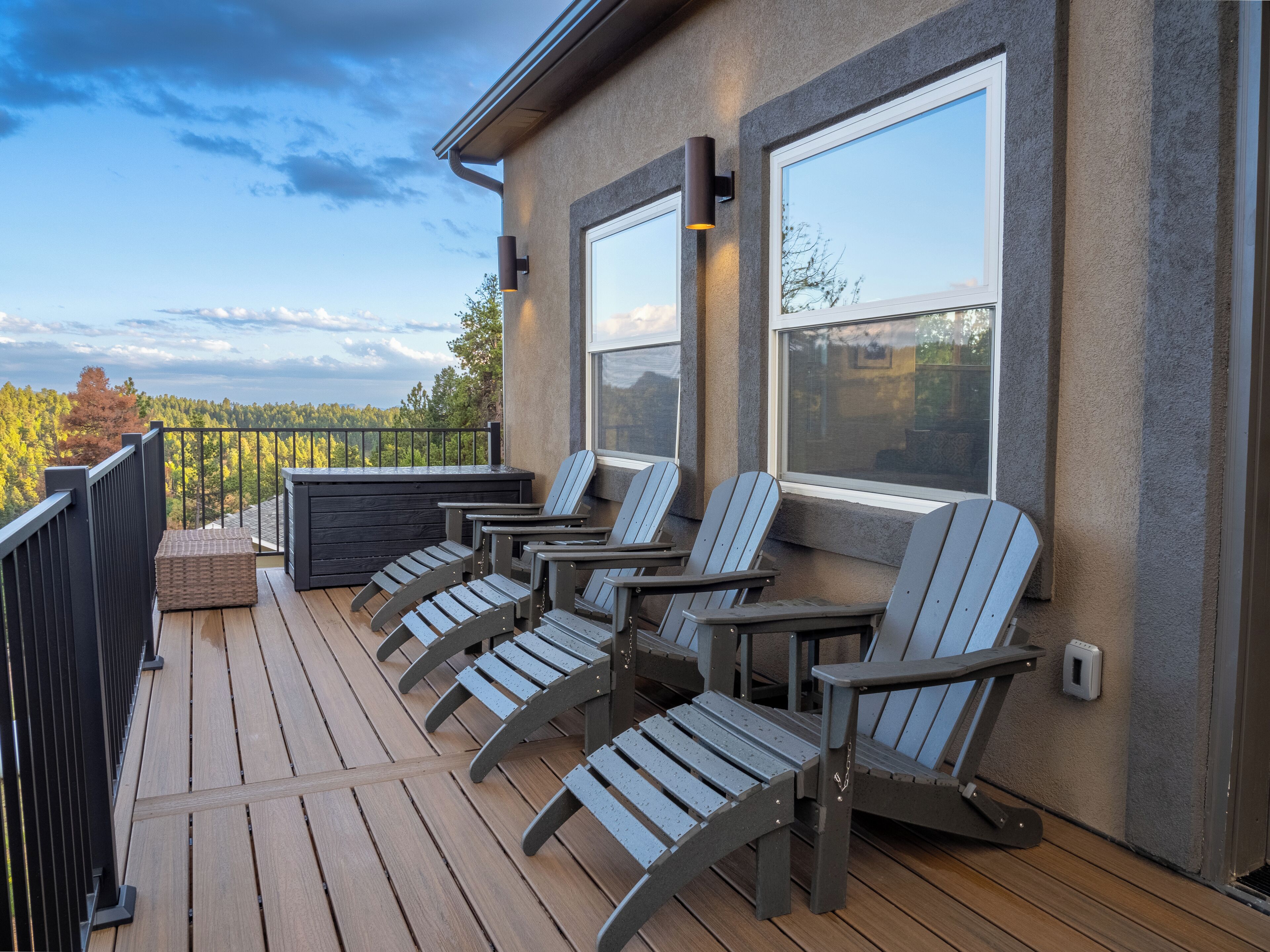 A deck with four Adirondack chairs, a small table, and a black railing.