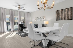 Ein moderner Essraum mit einem weißen Tisch und Stühlen, einem Deckenventilator und einer Chandelier.