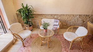 Une pièce avec des chaises en osier, une table en verre, une plante en pot et un mur en pierre.
