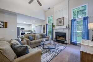 A living room with a fireplace, a sofa, a coffee table, and a view of the kitchen. - Pet-friendly 3BR w Porch & Grill Weekday Deals! (Woodstock)