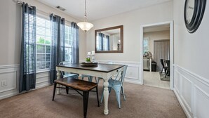 A dining area with a wooden table, blue chairs, a chandelier, and a mirror on the wall. - Pet-friendly 3BR w Porch & Grill Weekday Deals! (Woodstock)