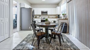 A modern kitchen with white cabinets, a stainless steel refrigerator, and a dining area with a round table and chairs. - Pet-friendly 3BR w Porch & Grill Weekday Deals! (Woodstock)