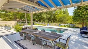 Un espacio exterior techado con piscina, terraza de madera y mobiliario exterior.