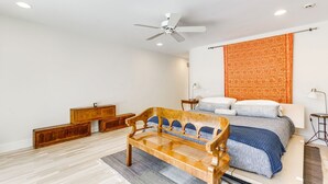Un dormitorio con una cama, un banco de madera, un ventilador de techo y un tapiz decorativo en la pared.