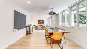 Un comedor amplio con una larga mesa de madera y sillas amarillas, ventanas grandes en un lado y una pizarra en la pared opuesta.