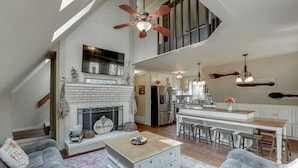 Amplia sala de estar estilo loft con chimenea, una cocina con barra y una escalera que sube a un nivel superior.