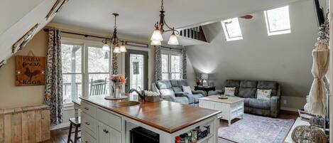 A cozy kitchen with a central island, white cabinetry, and a rustic ceiling. There is a dining area with a leather sofa and a small table.