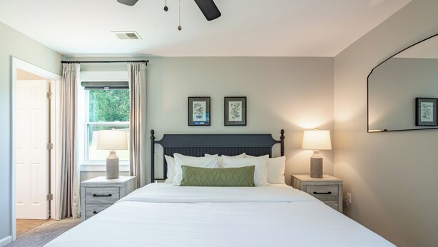 A bedroom with a large bed, two bedside tables with lamps, a ceiling fan, and a window with curtains. - Pet-friendly 3BR 2BA Quiet Comfort Near Nature (Rydal)
