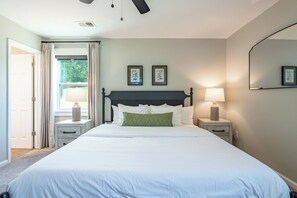 Ein Schlafzimmer mit einem großen Bett, zwei Nachttischen mit Lampen, einem Deckenventilator und einem Fenster mit Vorhängen.