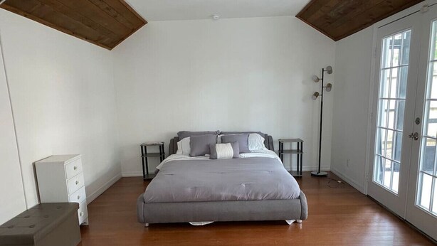 Un dormitorio con una cama grande, una mesita de noche, una lámpara de pie y un ventanal.