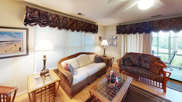 A living room with wicker furniture, a glass coffee table, and a view of the outdoors. - River Creek 1 Unit 401 (Sunset Beach)