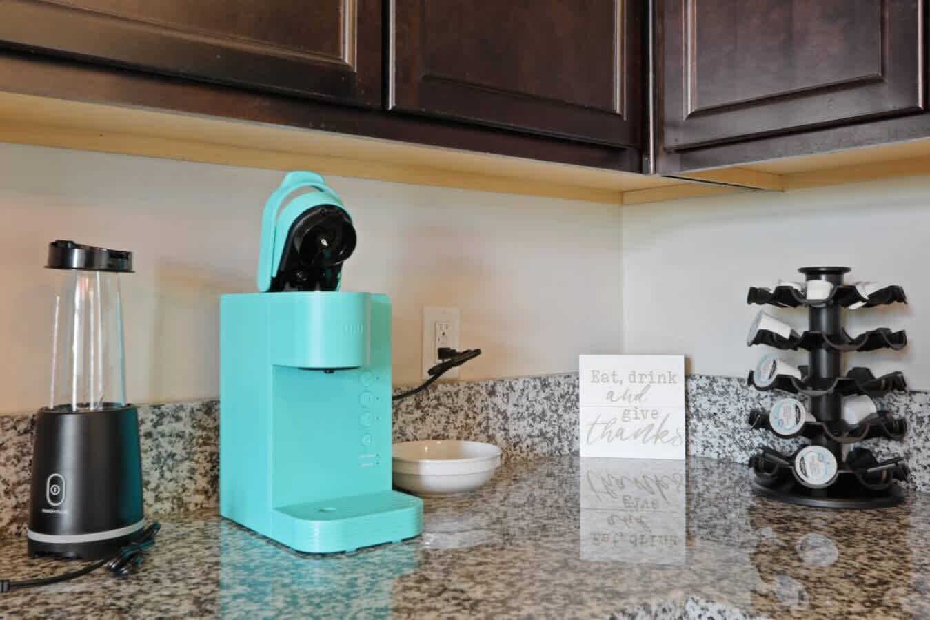 A kitchen with a coffee maker, a mug, and a sign that says "Eat, drink and give thanks."
