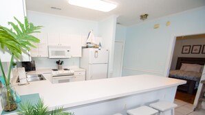 A compact kitchen with white cabinets, a central island with stools, a microwave, stove, and refrigerator. - River Walk 304 (Myrtle Beach)