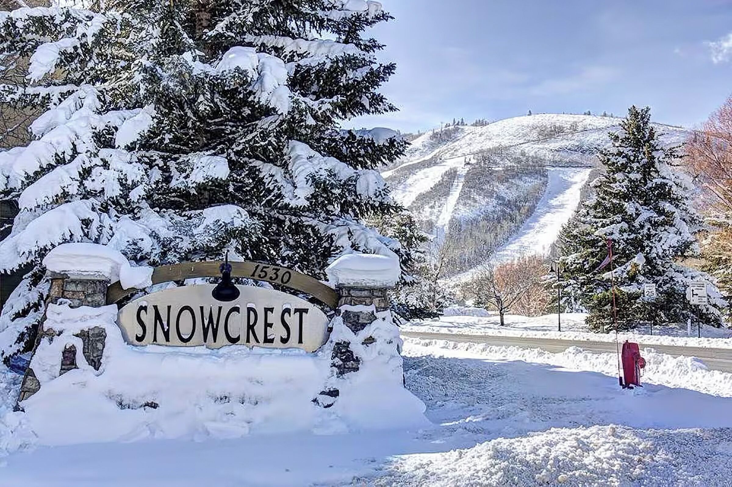 Ein schneebedecktes Schild mit dem Schriftzug 'Snowcrest' und eine Steinmauer.