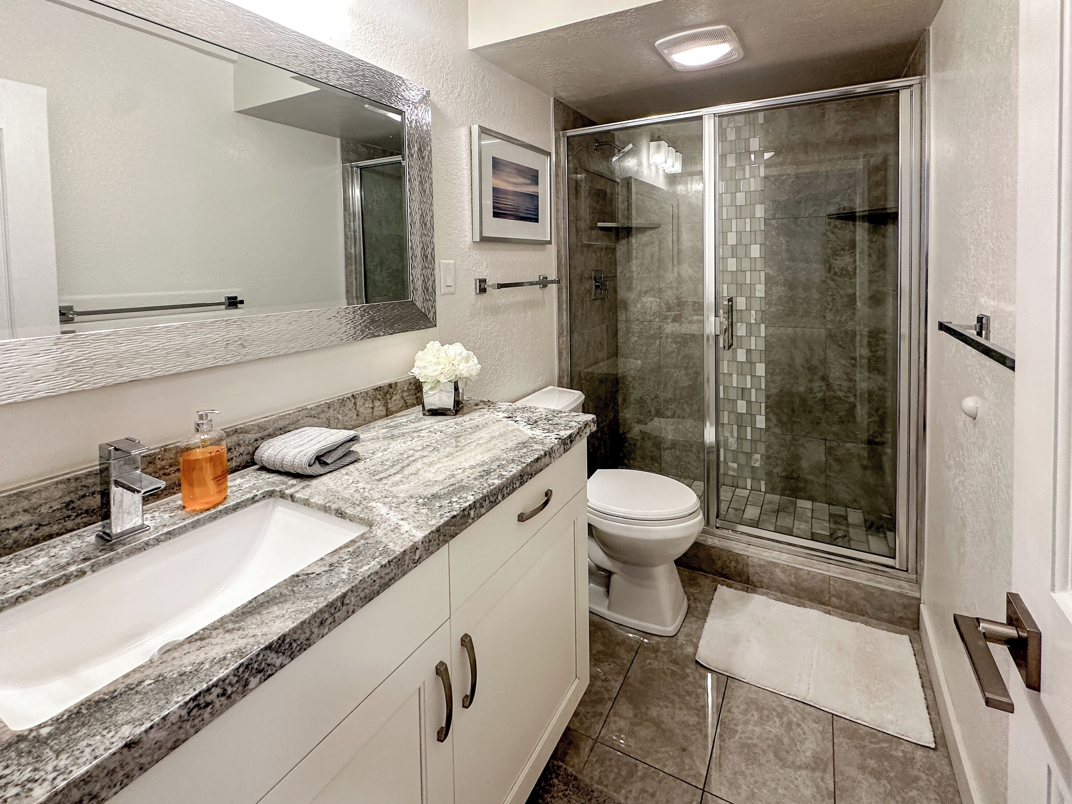 Een badkamer met een marmeren aanrecht, een douchecabine van glas en een wit toilet.