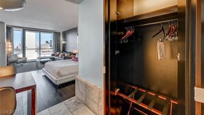 Ein modernes Hotelzimmer mit einem großen Bett, einem Schreibtisch und Blick auf die Stadt. Es gibt einen separaten Bereich mit Kleiderständer und Kleidung.