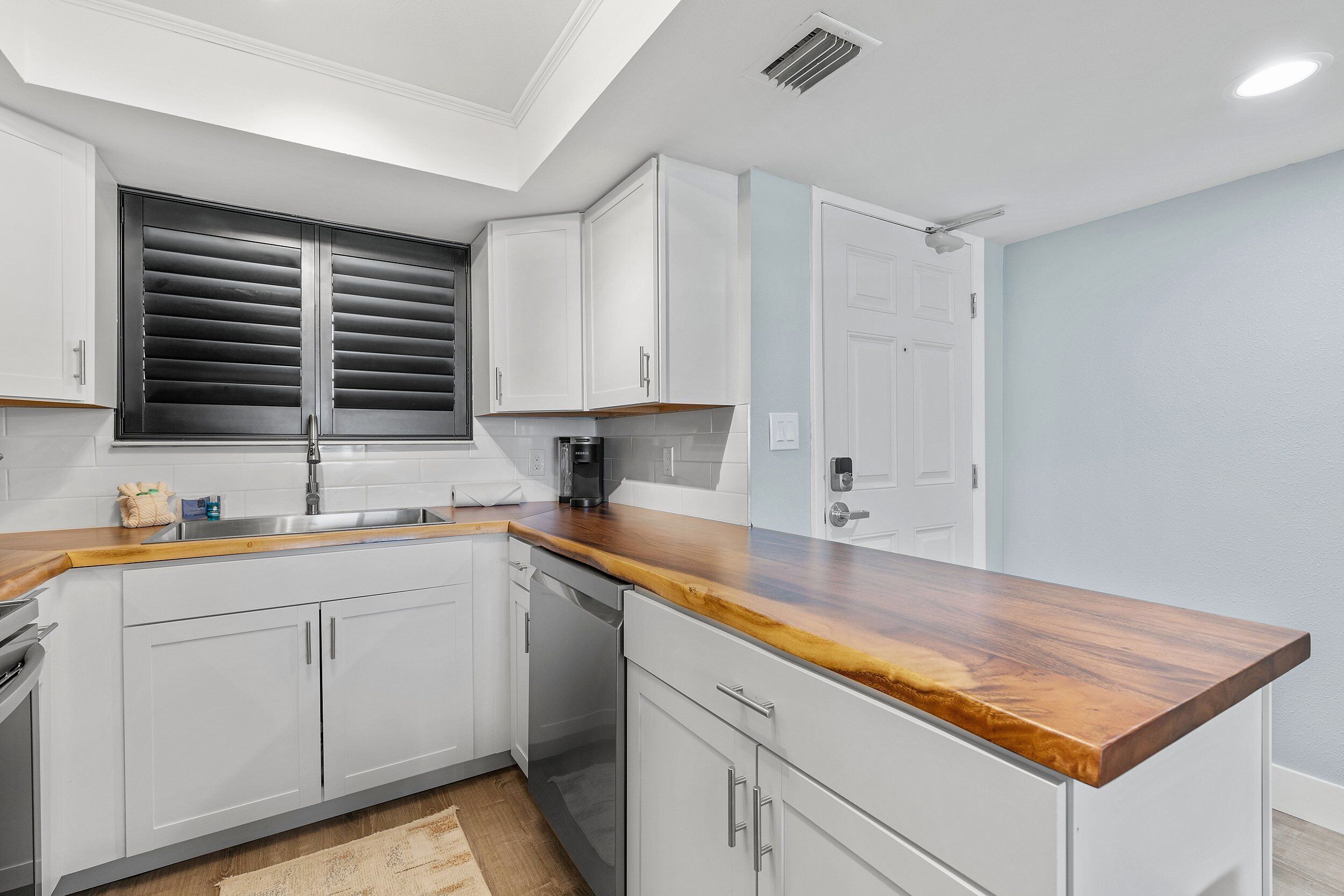A modern kitchen with white cabinets, a wooden countertop, and a built-in dishwasher.