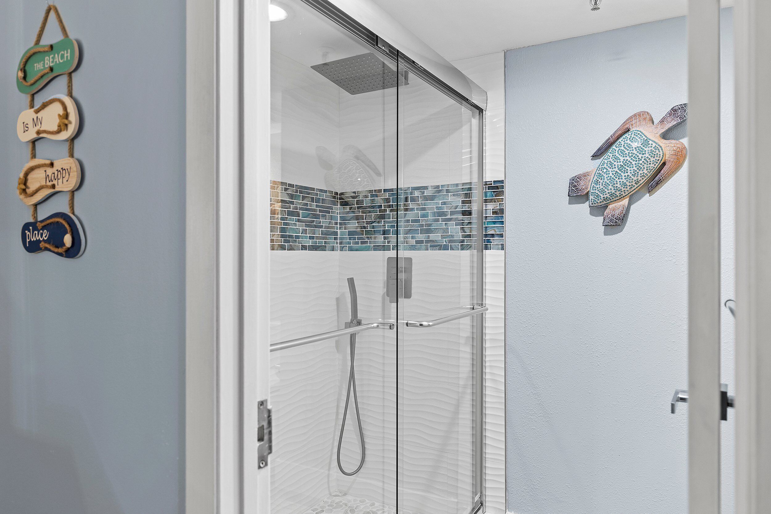 Ducha envuelta en vidrio con cabezal de ducha tipo lluvia, puerta de vidrio y borde de mosaico.
