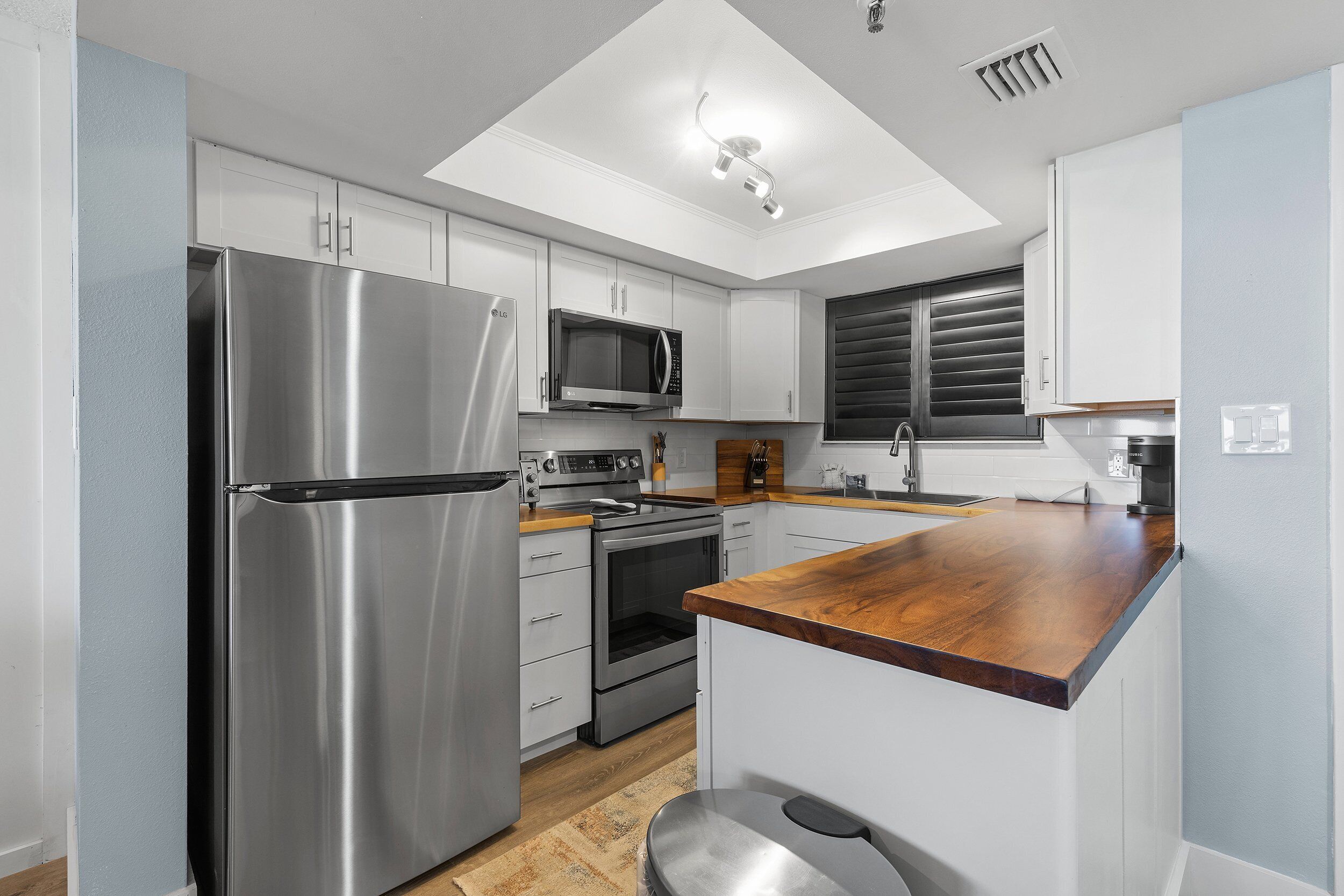 A modern kitchen with stainless steel appliances, white cabinets, and a wooden countertop.