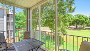 A covered outdoor area with a table and chairs, a view of a green lawn and trees, and a metal railing. - Royal Poste Unit 3203 (Sunset Beach)